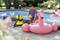 A man is inflating a large, pink flamingo pool float with a yellow device by the pool. Plants are visible in the background.