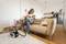 A person is vacuuming a sofa with a steam cleaner in a modern living room. A kitchen is visible in the background.