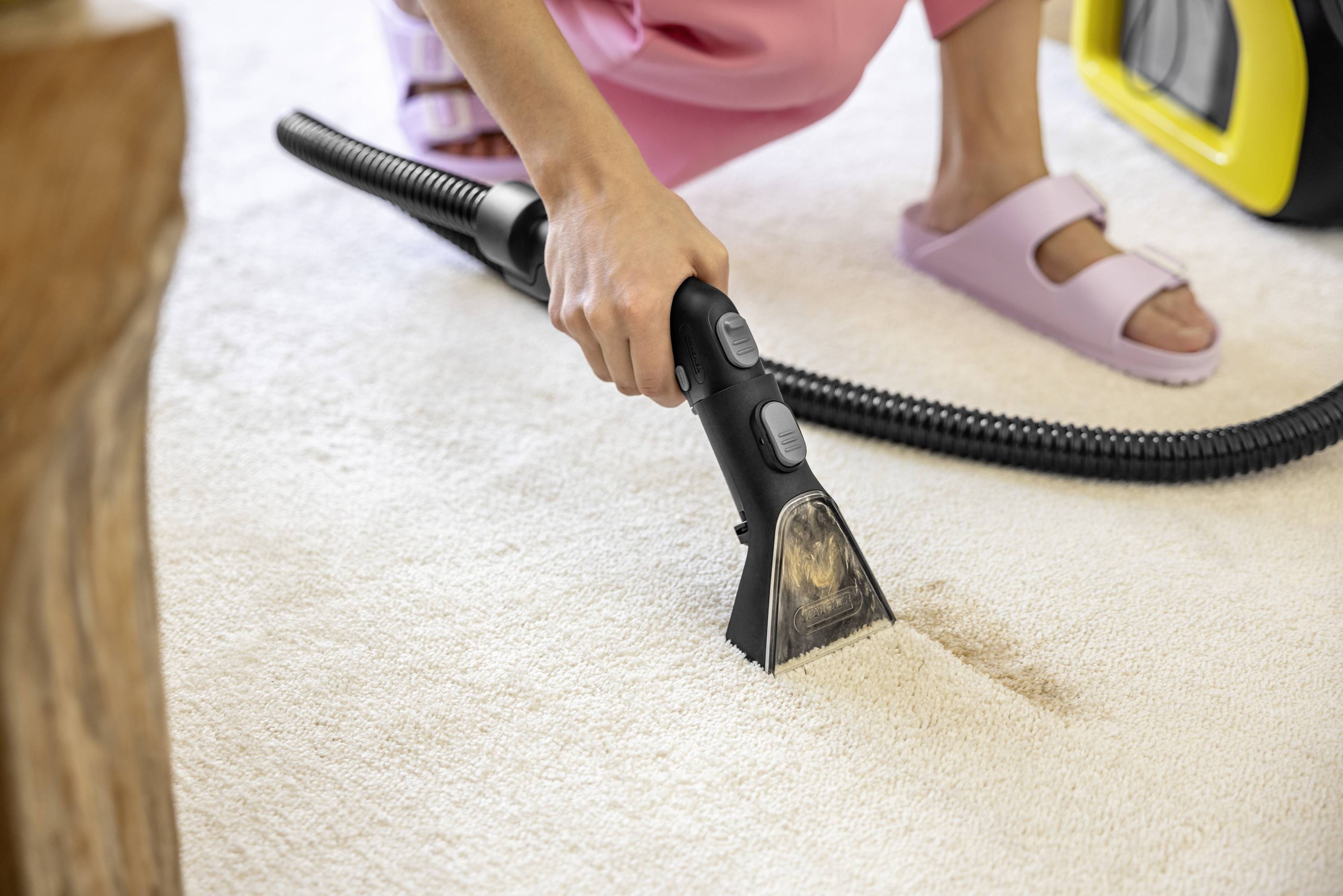 A person is cleaning a light-coloured carpet with a hoover and removing a stain. Close-up view of the hand and nozzle of the device.