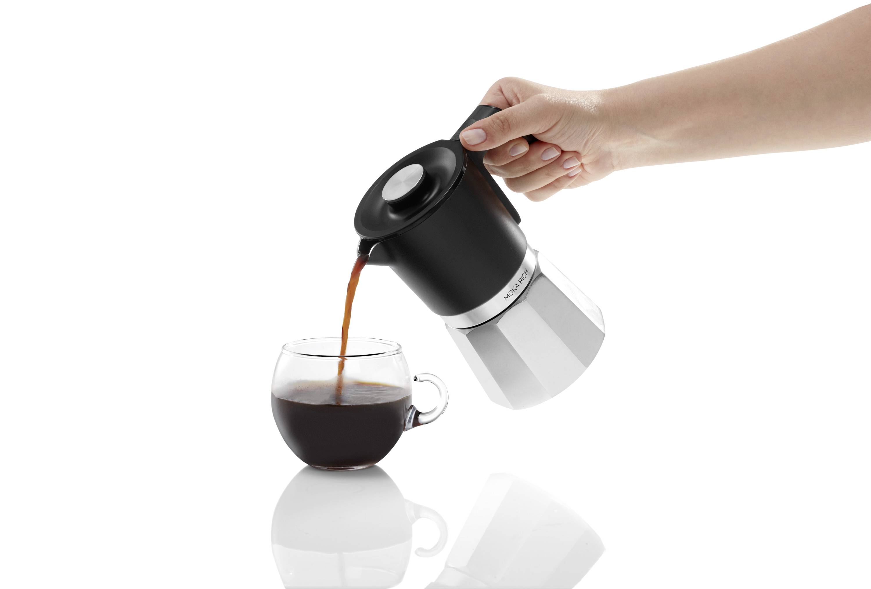 A hand is pouring coffee from a silver and black espresso pot into a small glass cup.