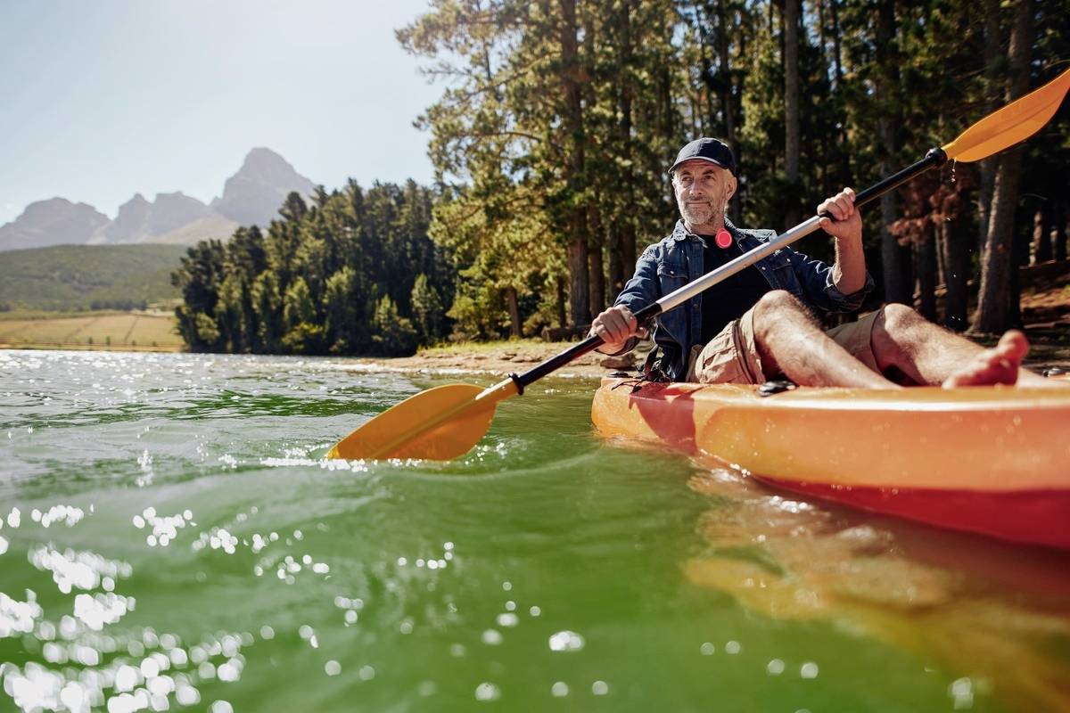 A person is paddling in an orange kayak on a tranquil lake, surrounded by trees and mountains in the background.