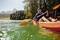 A person is paddling in an orange kayak on a tranquil lake, surrounded by trees and mountains in the background.