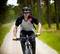 A man is cycling along a forest path. He is wearing a helmet and protective clothing, surrounded by green trees and nature.
