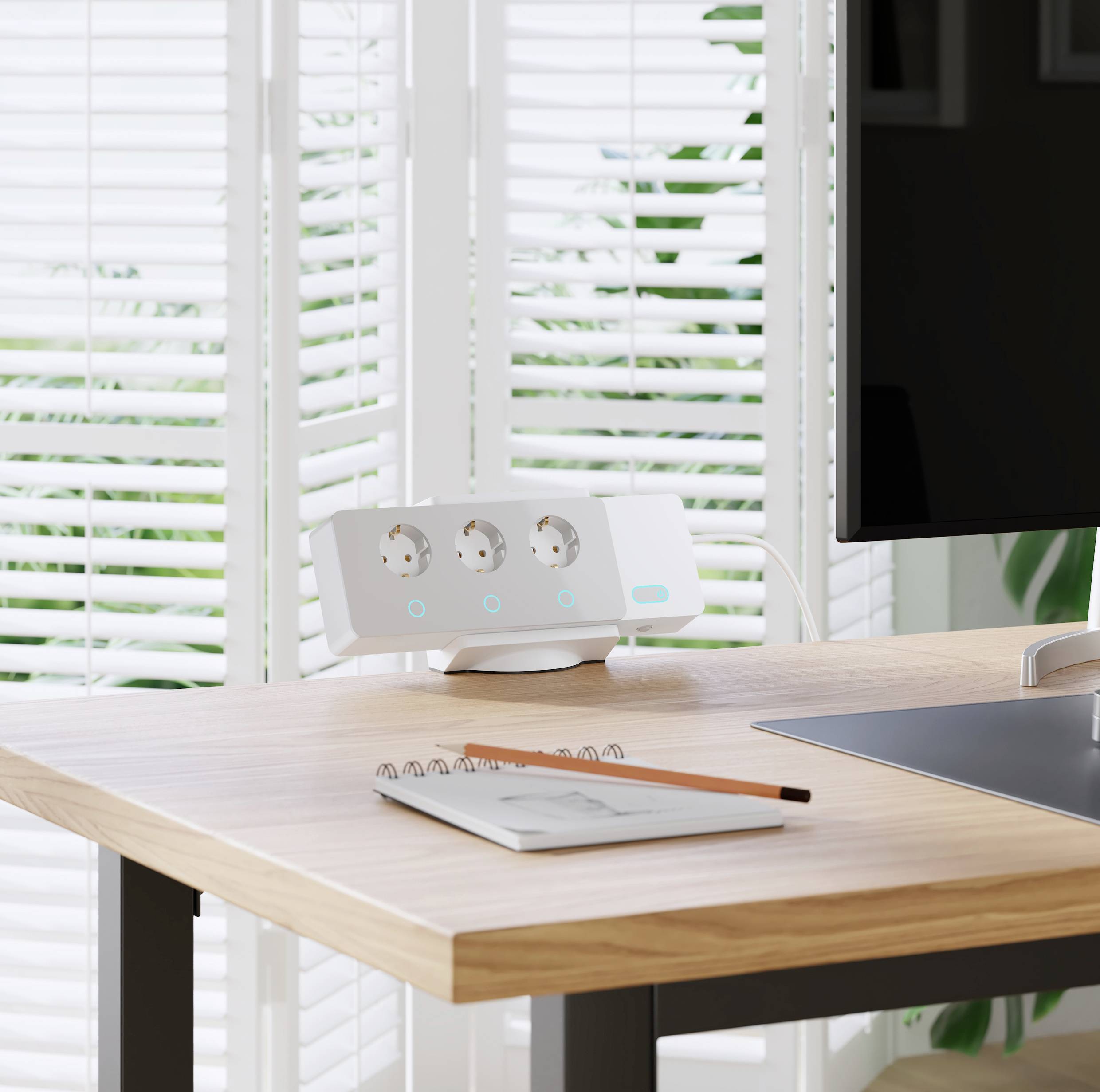 A desk with a laptop, pen, and notepad. In the background, there is a multi-socket extension lead with three sockets.