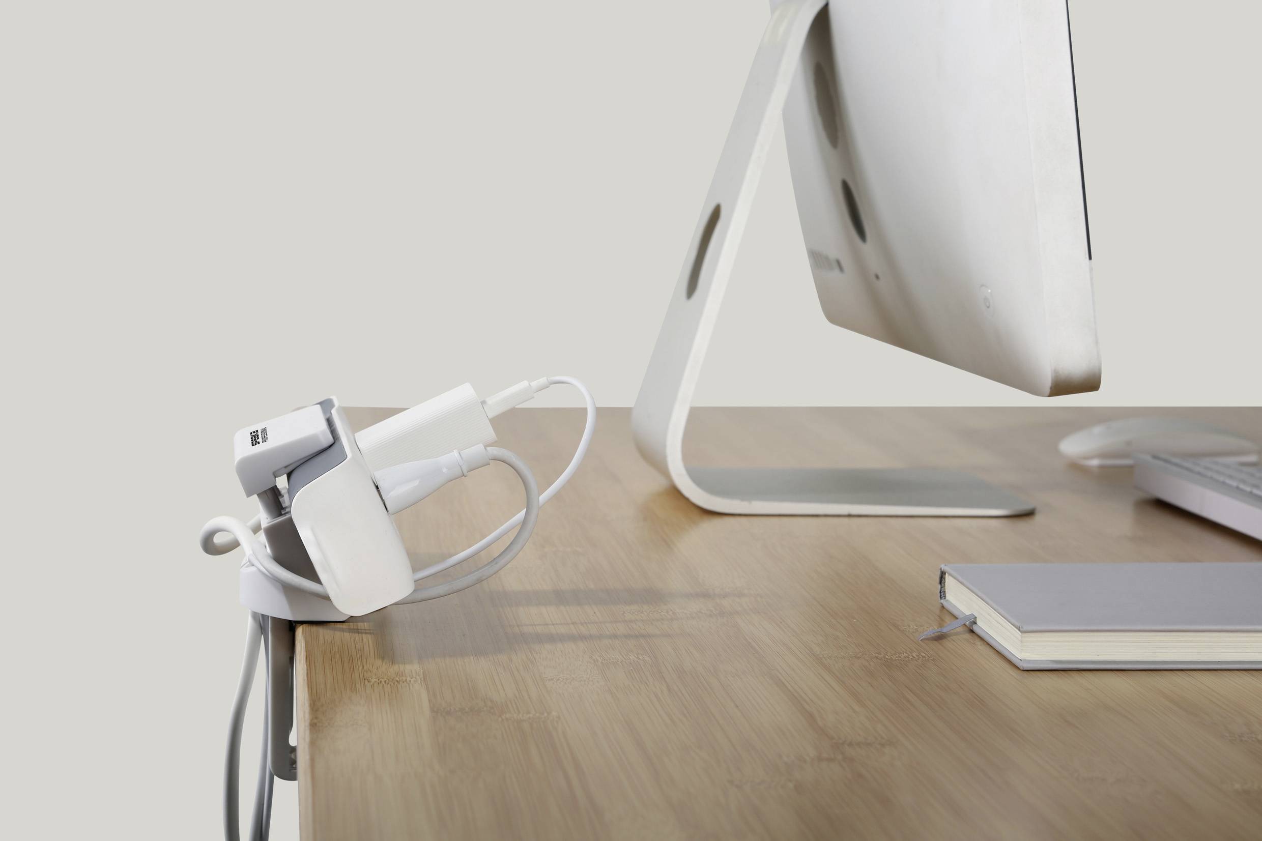 A computer monitor on a desk with a notebook and cable management solutions that neatly organise cables.