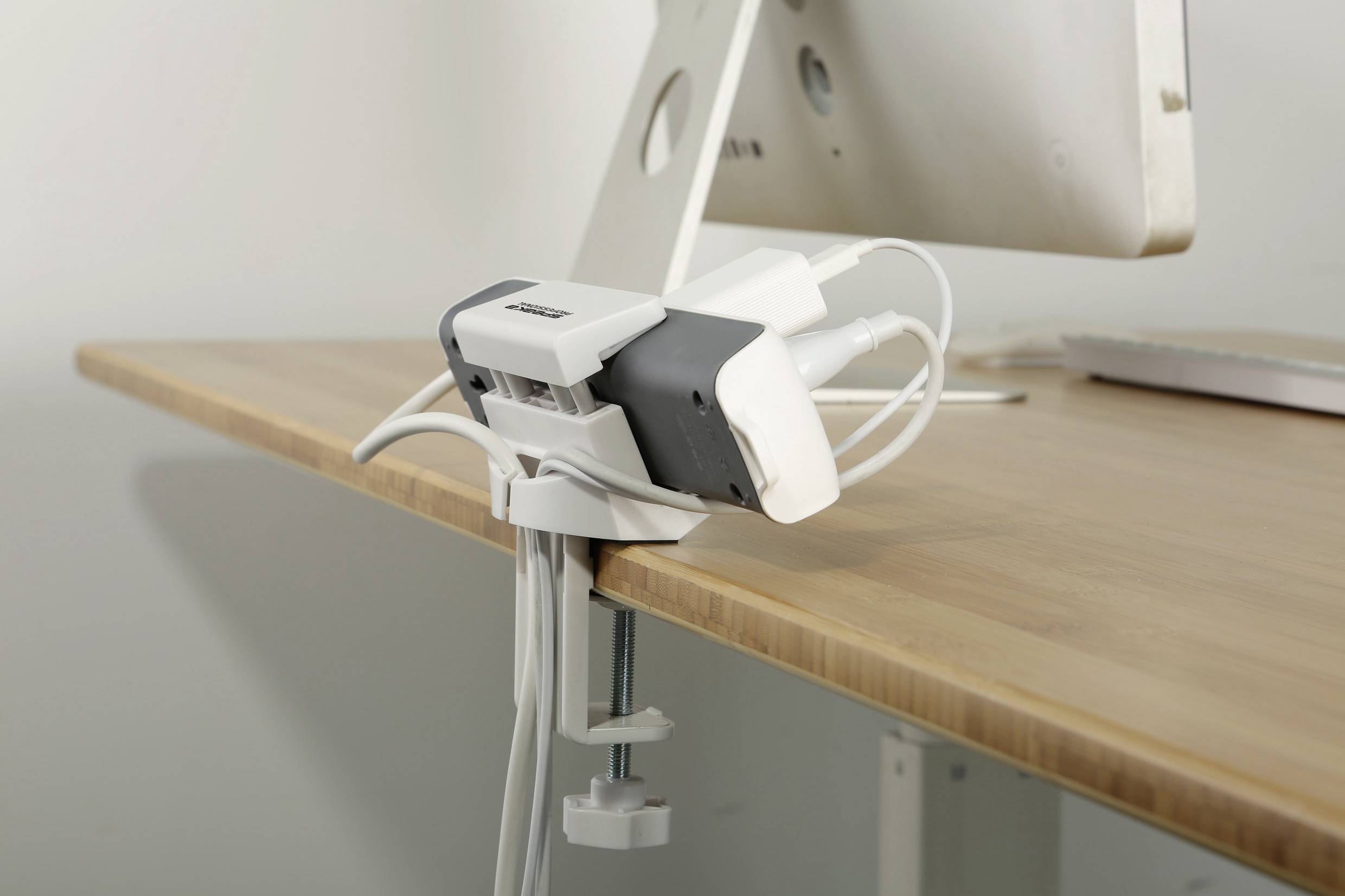Multiway power strip attached to a desk, cable management solution for electronic devices.
