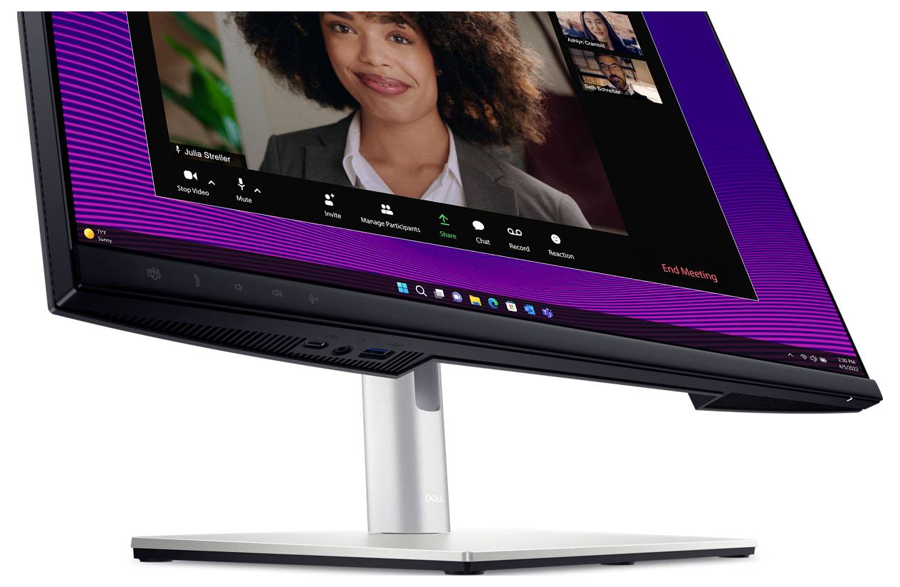 A desktop monitor displays a video conferencing tool showing a woman in conversation. Below are icons for participant management and ending the meeting.