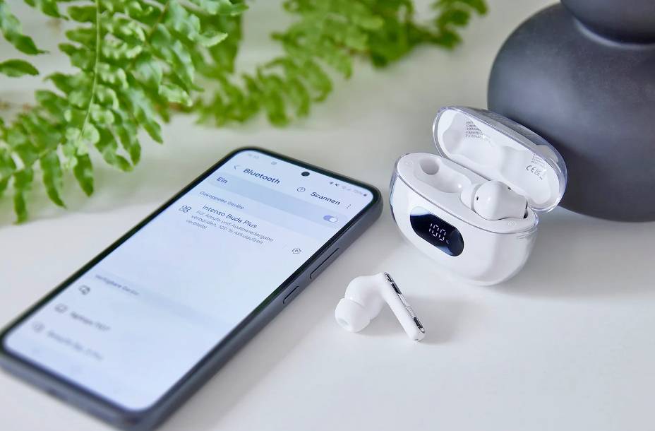 Smartphone next to a white wireless earbuds set in an open charging case on a table; Bluetooth connection is shown on the mobile phone.