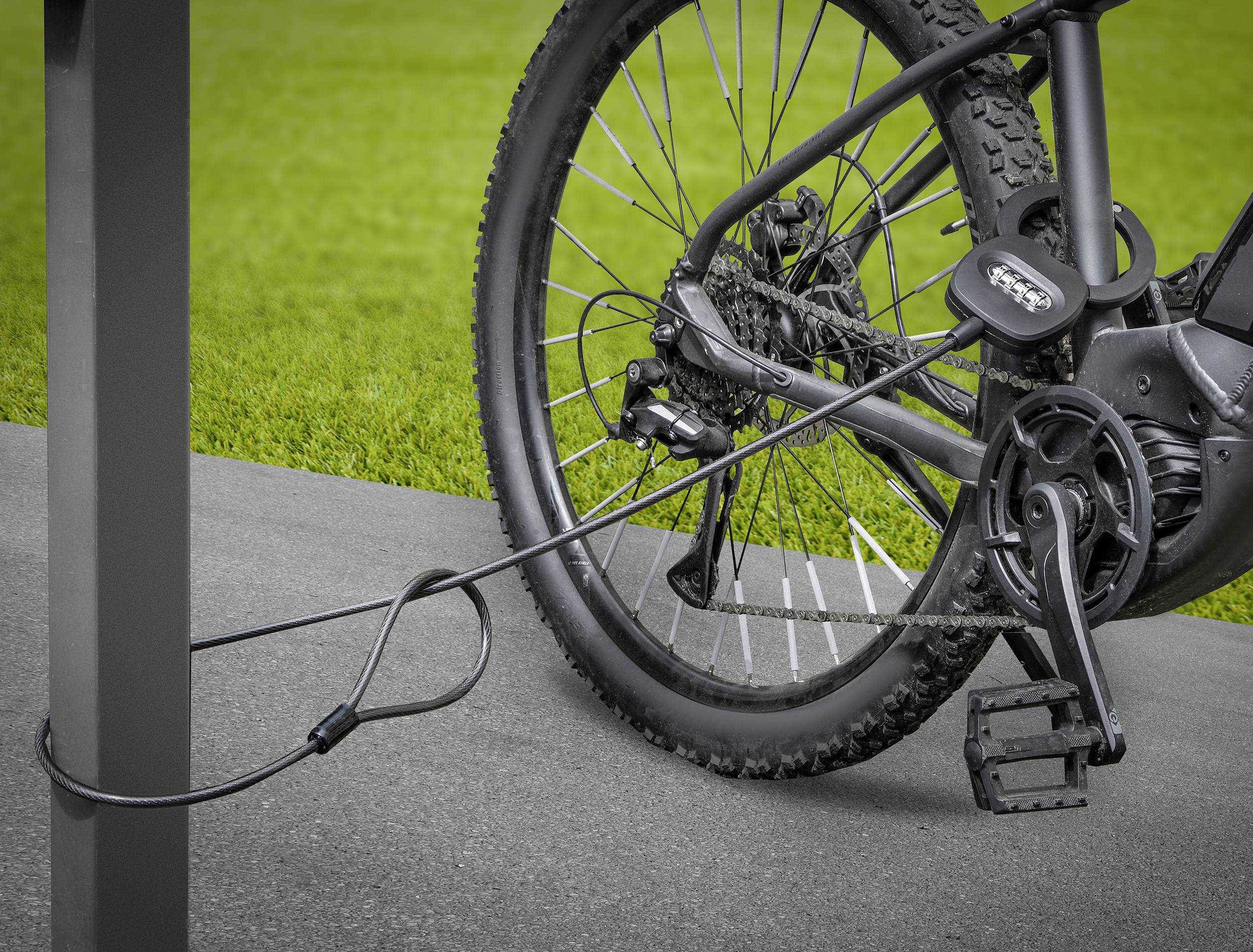 Part of a bicycle secured with a lock at a bike rack, with a grassy area in the background.