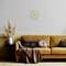 A living room with a yellow sofa, decorative cushions, a throw, a vase with dried flowers, and a wall clock.