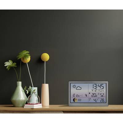 A digital weather and time display on a wooden table with green and pink vases. Time: 13:45. Weather: Sunny, 20°C.