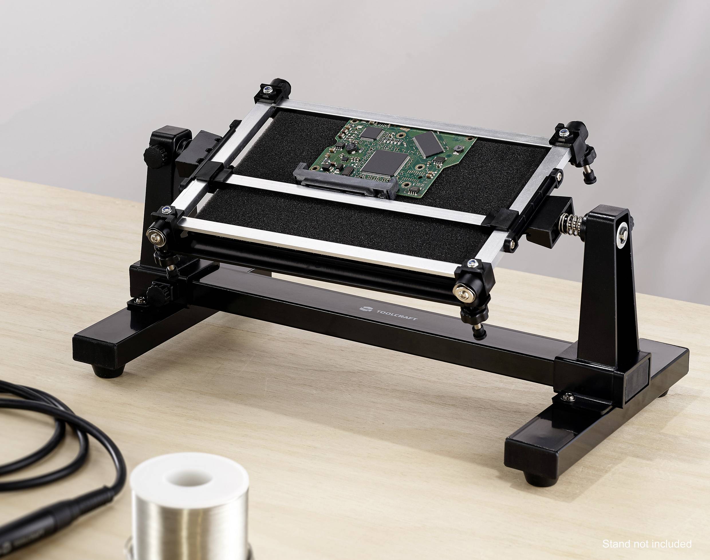 A circuit board holder with a mounted printed circuit board on a table. A cable and solder are lying beside it.