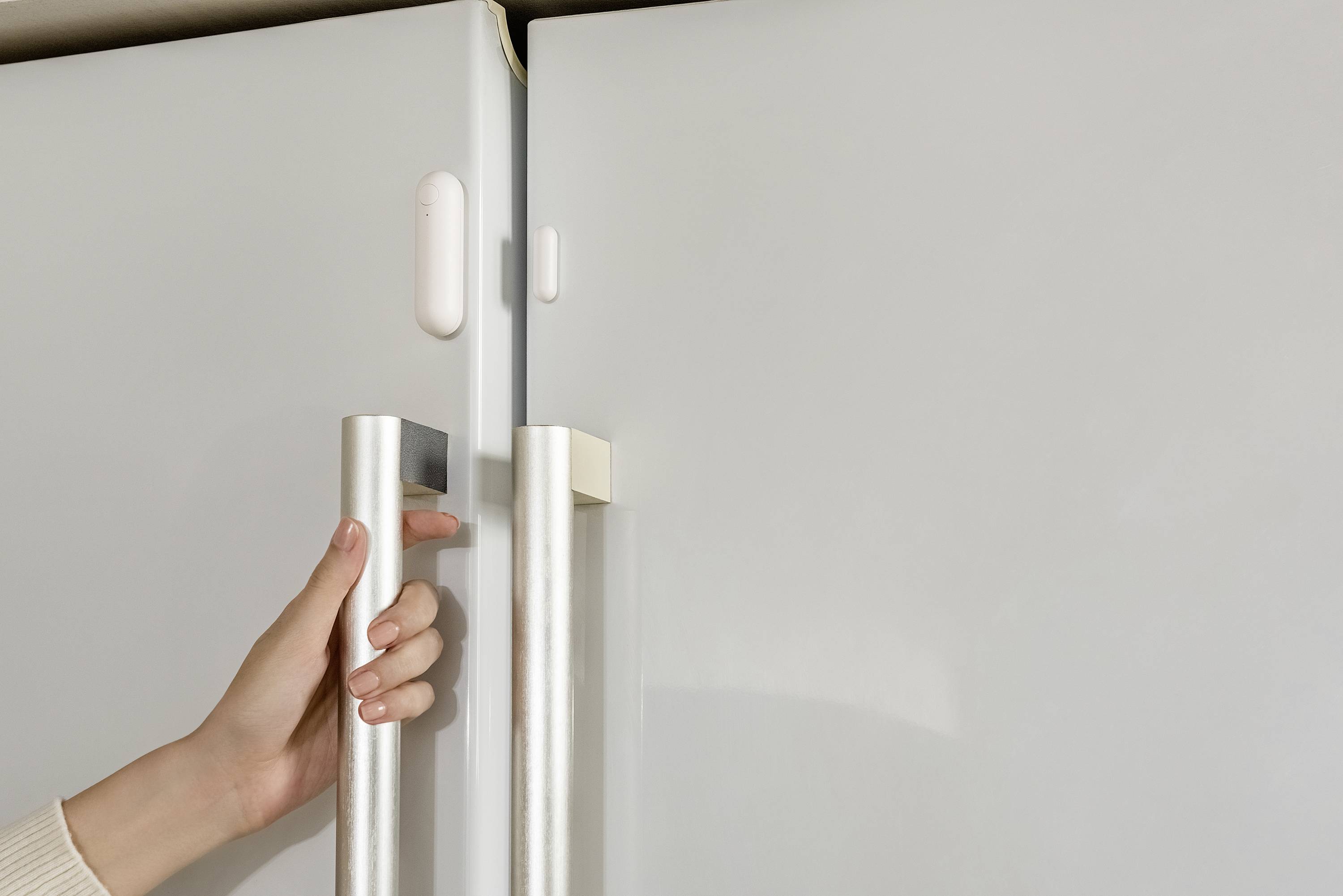 A hand opens the door of a white fridge.