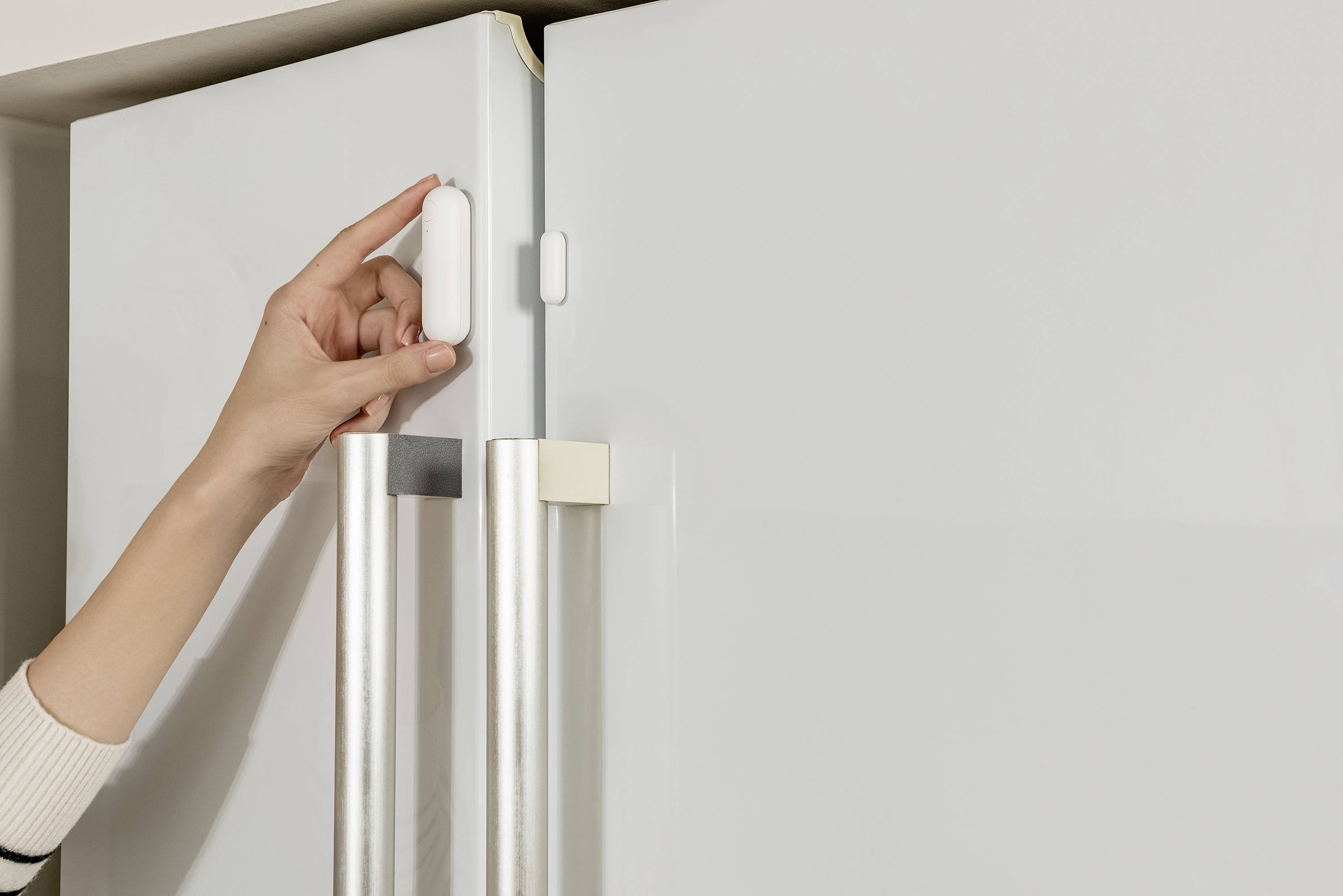 A hand opens a fridge with double doors. A safety lock is attached to one door, ensuring child safety.