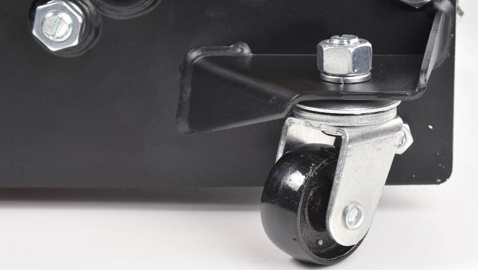 A close-up of a metal swivel caster attached to the corner of a black piece of equipment, highlighting the wheel and mounting bracket.