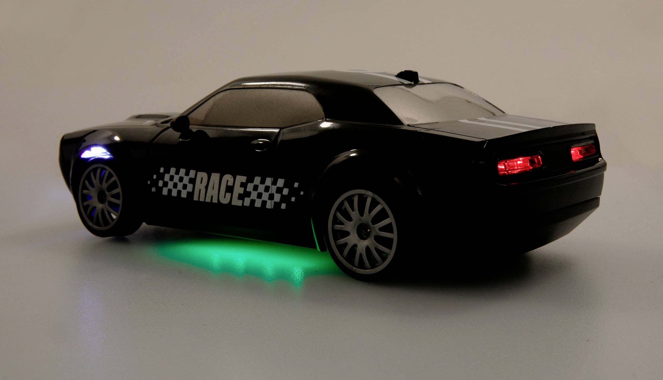 Black toy car with 'RACE' lettering, illuminated rear lights, green underbody lighting on a grey background.
