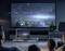 A family sits in a dimmed room, watching a science fiction scene with light beams on a large television, while a laptop on the table displays the same image.