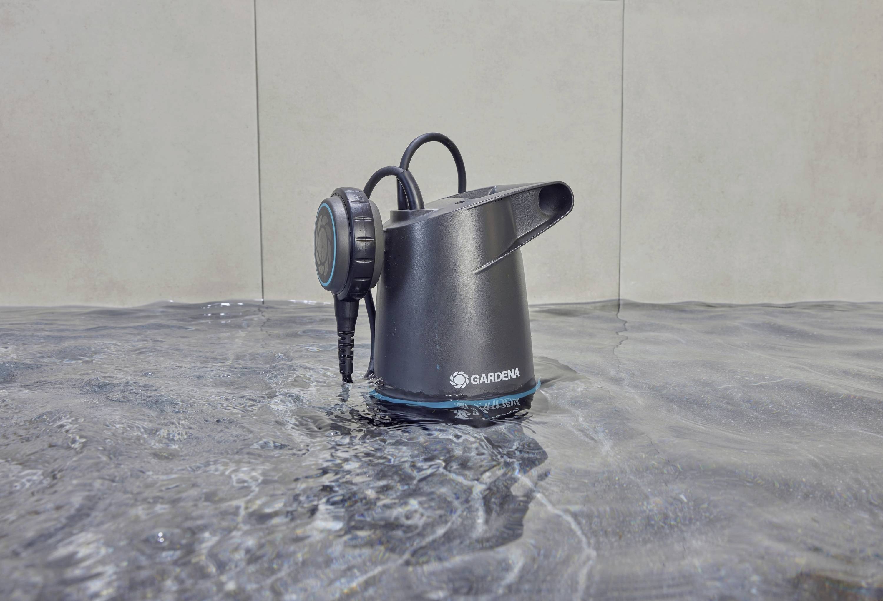 Black water pump sits in shallow water. "Gardena" logo visible on the pump. Used for irrigation or water transfer.