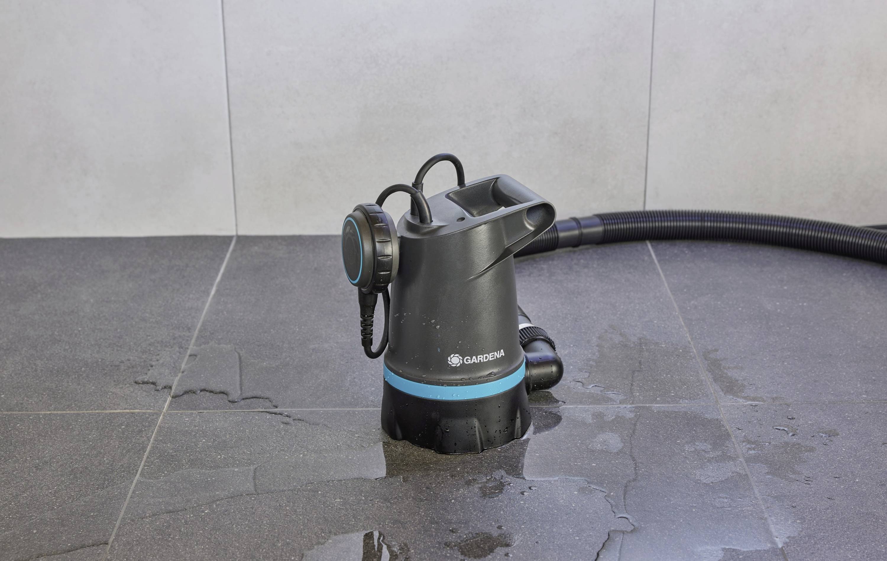 A black water pump is draining water from a waterlogged ground. A hose is connected to the pump to divert the water.