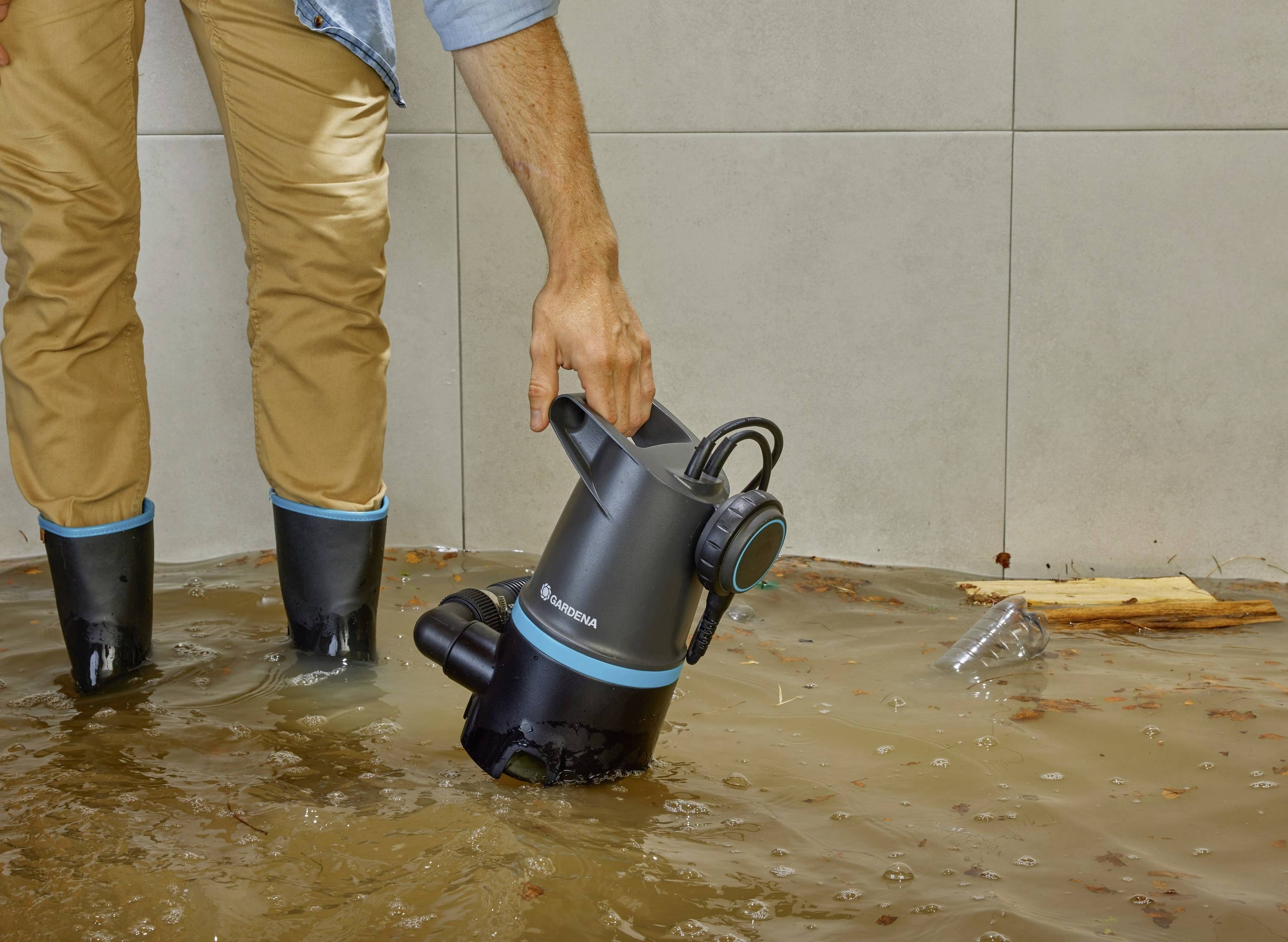 A person wearing wellington boots is using a submersible pump to drain contaminated water from a flooded room.