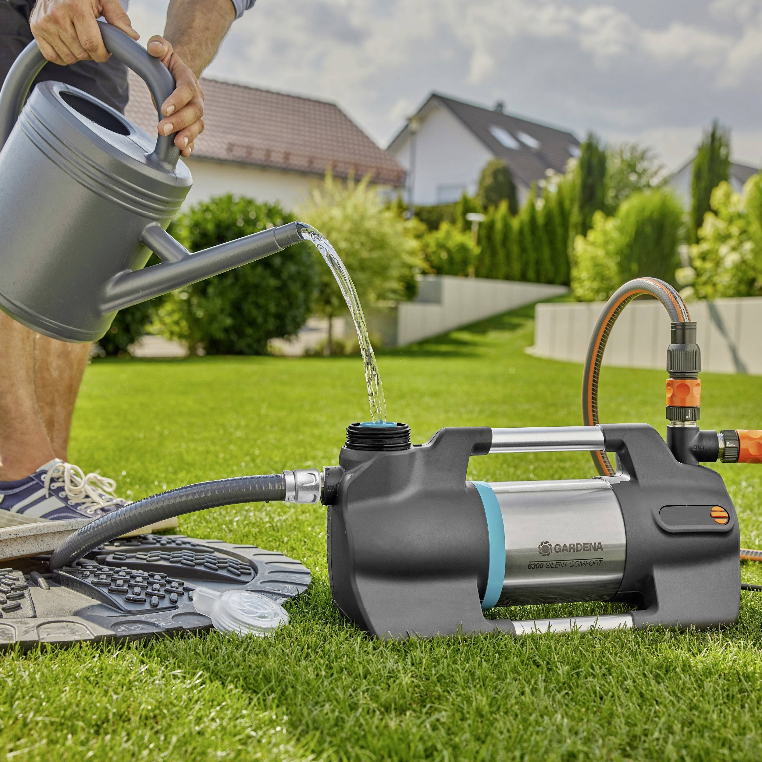 A person is watering a lawn with a watering can, with an electric water pump connected in the foreground.
