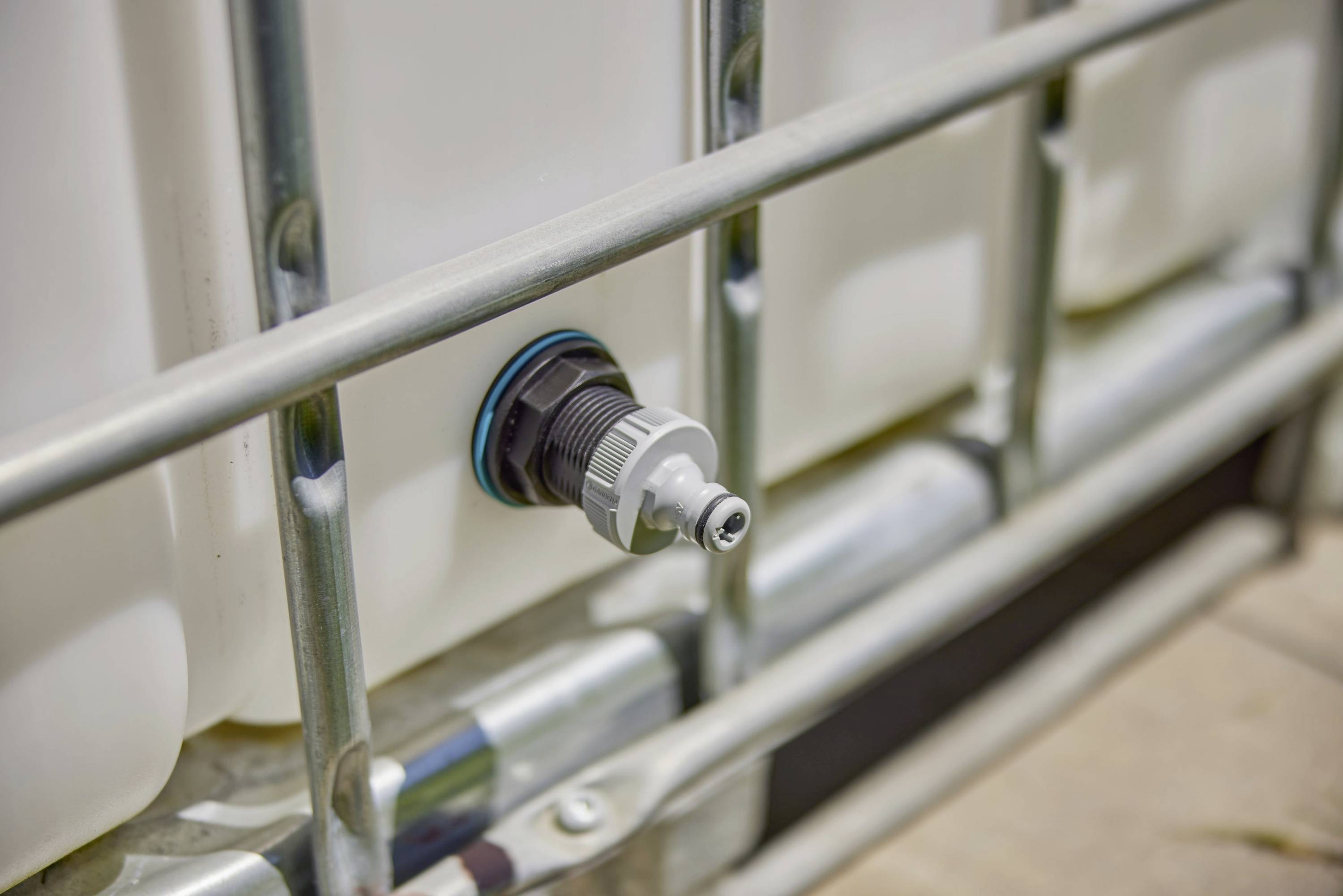 A white liquid tank with a silver valve and blue seal at the front, surrounded by a metal frame.