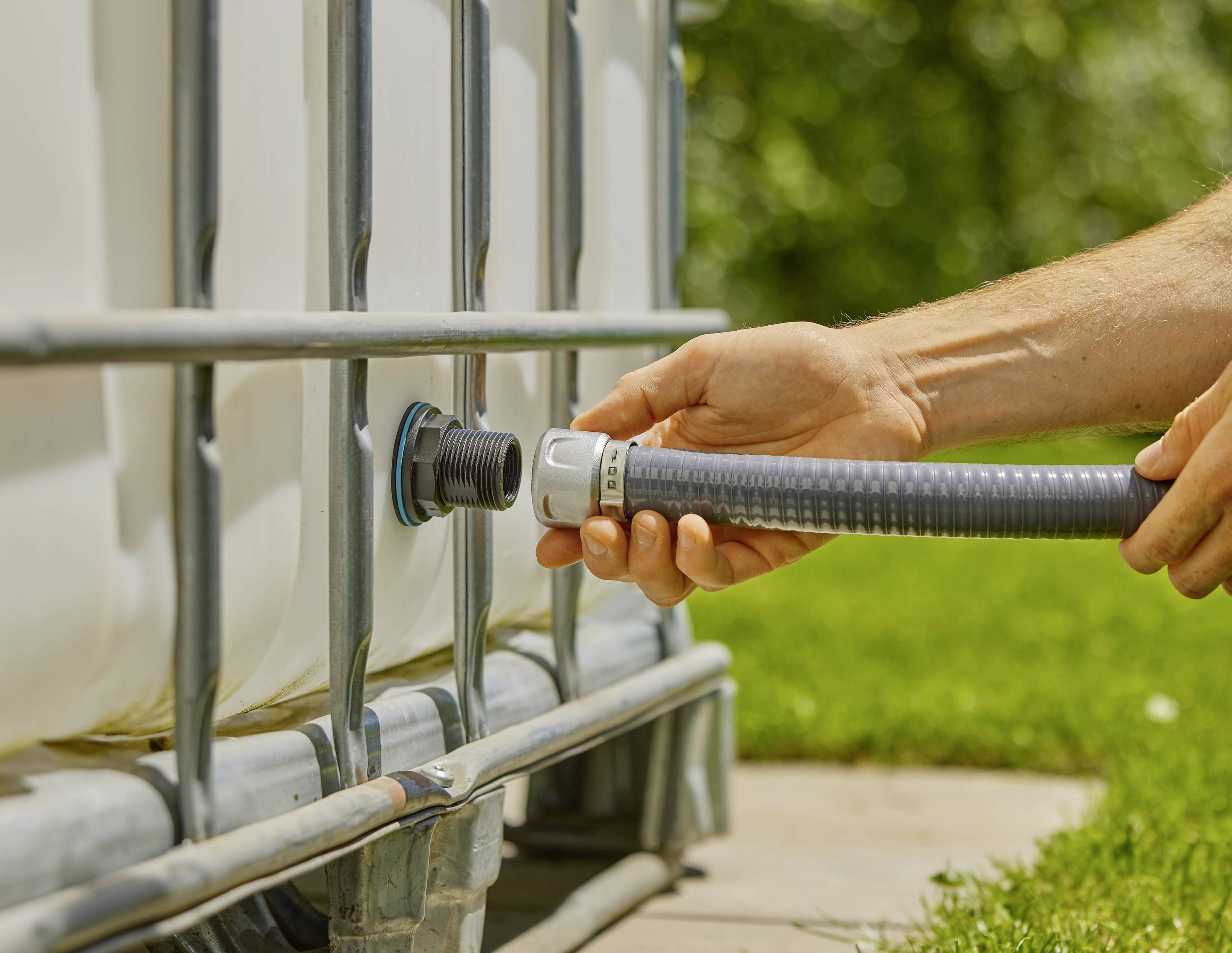 A person is connecting a hose to a large water tank outdoors. Grass can be seen in the background.