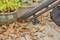 A leaf blower removes dry leaves from a wooden decking. Potted plants are positioned beside the foliage.