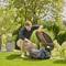 A man in the garden opens the lid of a robotic lawnmower. Surrounded by plants and trees on a sunny day.