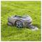 A robotic lawn mower is cutting grass autonomously on a green lawn. The device is sleek with a gray body and blue accents.