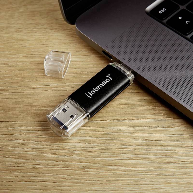 A USB stick with the label 'Intenso' is plugged into a laptop resting on a wooden table. The protective cap lies beside it.