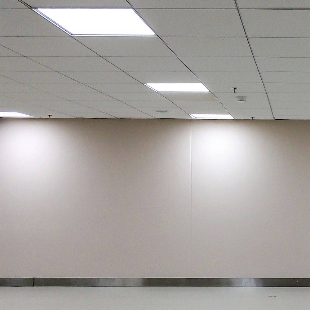 A bare, bright wall with a metal skirting board and white ceiling tiles.