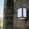 Wall light made of black metal and glass mounted on a stone wall, with a soft light glow. Surroundings show stone texture.