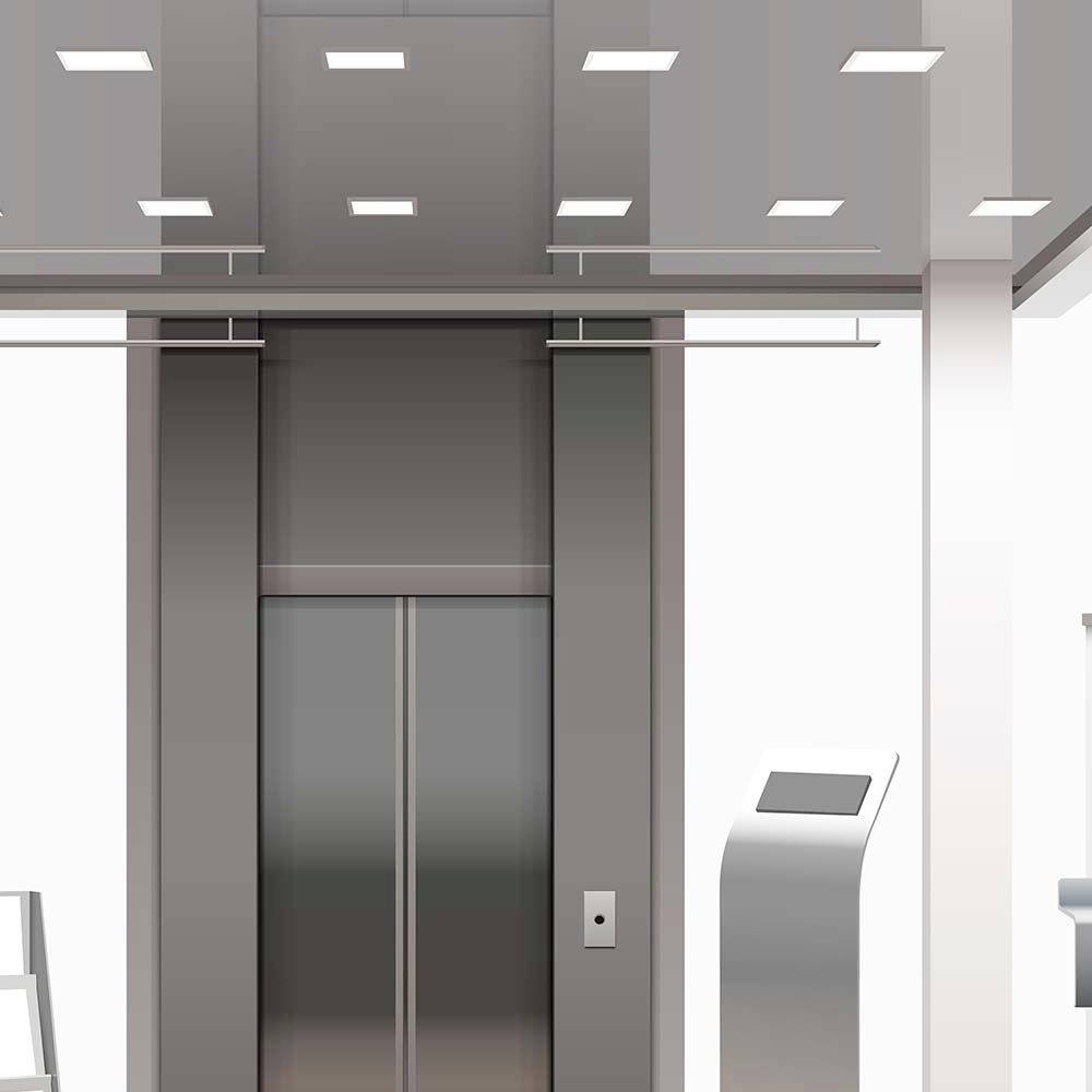 A modern lift in a building. The lift has closed doors and is illuminated by bright ceiling lights.