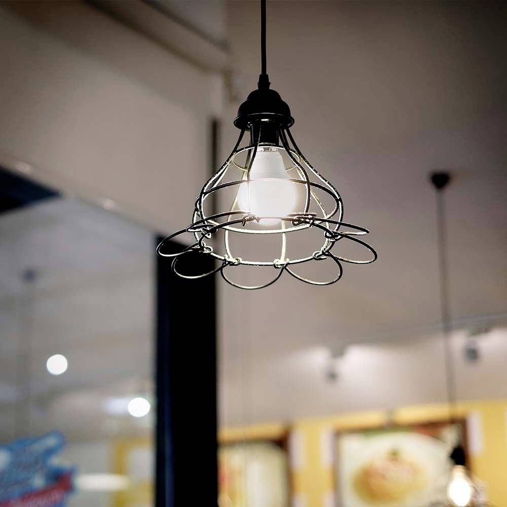 A stylish pendant light with a metal frame hangs from the ceiling in a modernly furnished room with a blurred background.