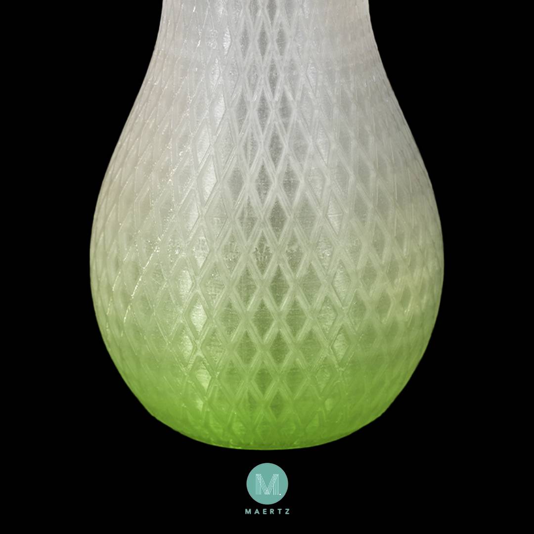 A vase with a pattern transitioning from white to light green, set against a black background. At the bottom, there is a round logo with "MAERTZ".