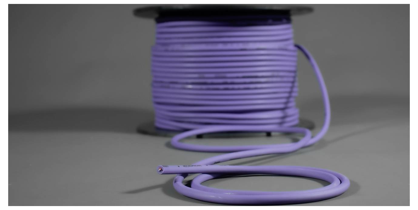 A large reel of purple cable, partially unwound and pulled forward. The cable is set against a grey background.