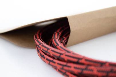 A red, braided cable protrudes from a brown paper bag. The cable has a black, geometric pattern.