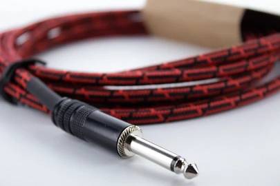 A red, patterned guitar cable with metal plugs is coiled up.
