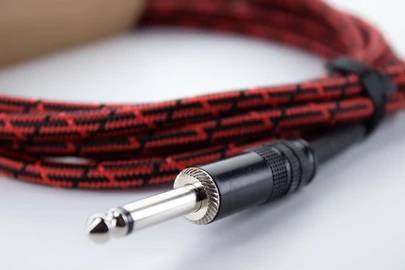 A red, patterned guitar lead with a 6.3mm jack plug is resting on a white surface.