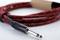A red, patterned guitar lead with a 6.35 mm jack plug is coiled on a surface.