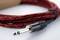 A jack cable with a red and black fabric sheath is lying on a table. It has a silver plug with a black handle.