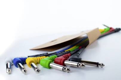 Several coloured audio cables with jack plugs lie side by side on a table, protruding from a cardboard packaging.