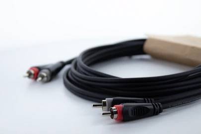 A black audio cable with RCA plugs, one marked red, laid out and ready on a white surface.