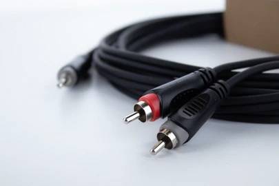 A long audio cable with two RCA plugs, one red and one white, is lying on a table. It is used for audio connections.