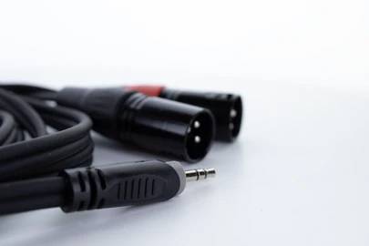 Black and red audio cable with XLR and jack plugs, lying on a white surface. Used for sound transmission.