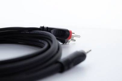 An audio cable with two RCA plugs, in red and black colours, is coiled on a white surface.
