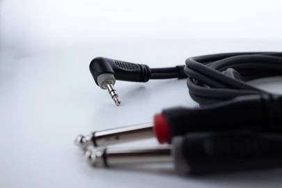 A black audio cable with two 6.35 mm jack plugs at the front and a 3.5 mm jack plug at the back, placed on a white surface.