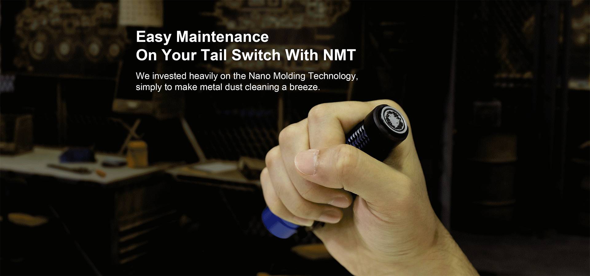 One hand holds a torch, with a workshop in the background. Text: 'Easy Maintenance On Your Tail Switch With NMT'.