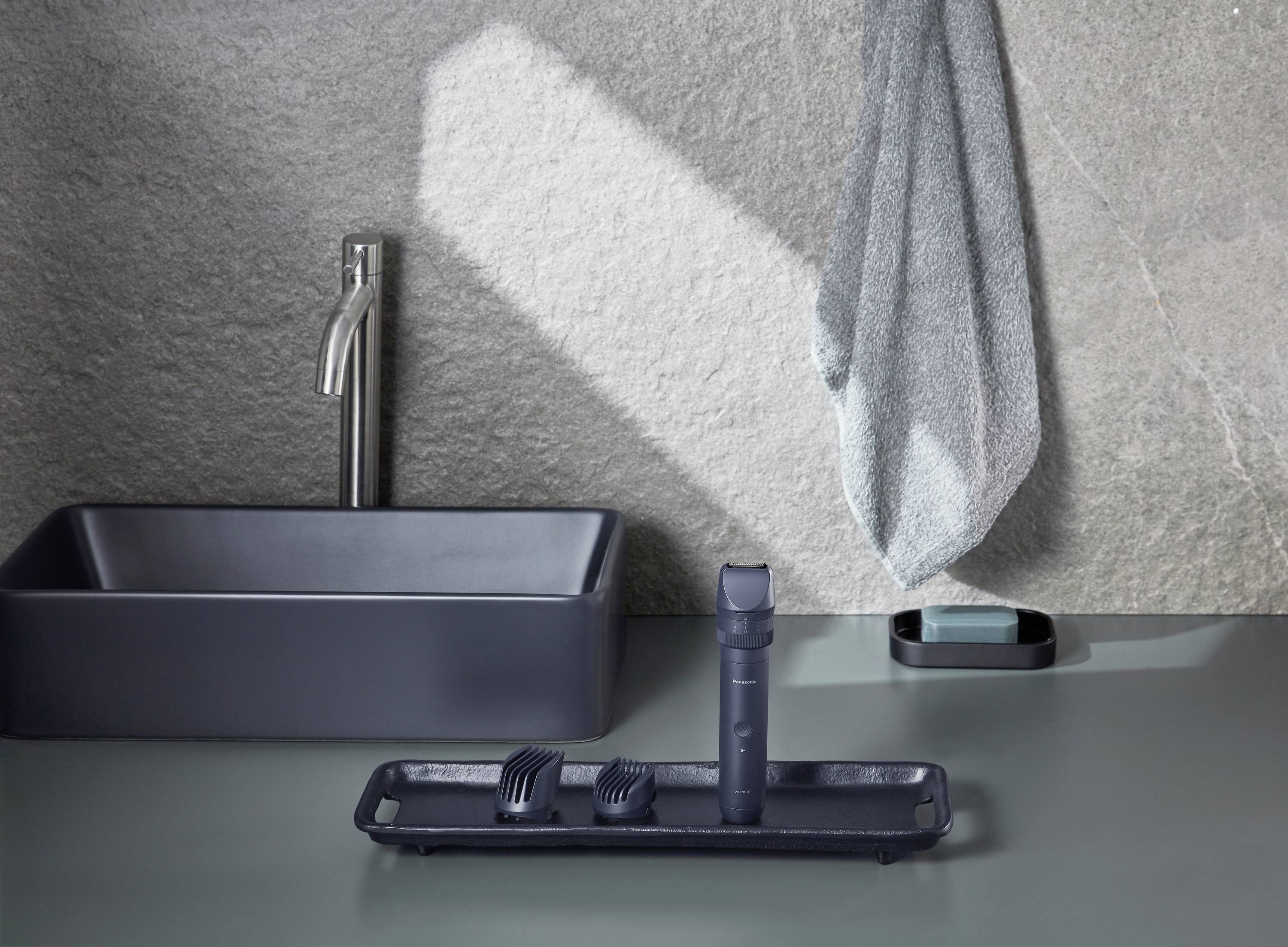 A modern bathroom with a grey washbasin, an LED mirror and a set of grey toothbrushes on a tray.